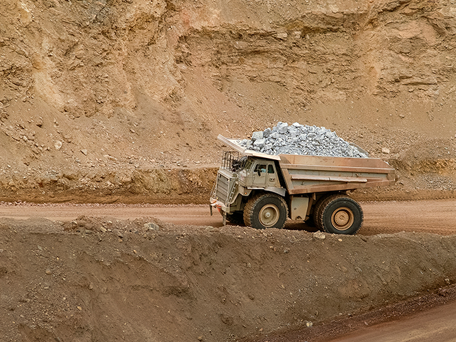 A large mining haul truck carrying a load of rocks drives along a dirt road in an open-pit mine.