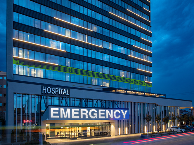 A modern hospital building at night with a brightly lit emergency entrance.