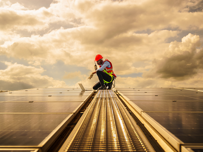 A worker on top of PV solar panels speaking into a handheld device with a laptop open in front of him